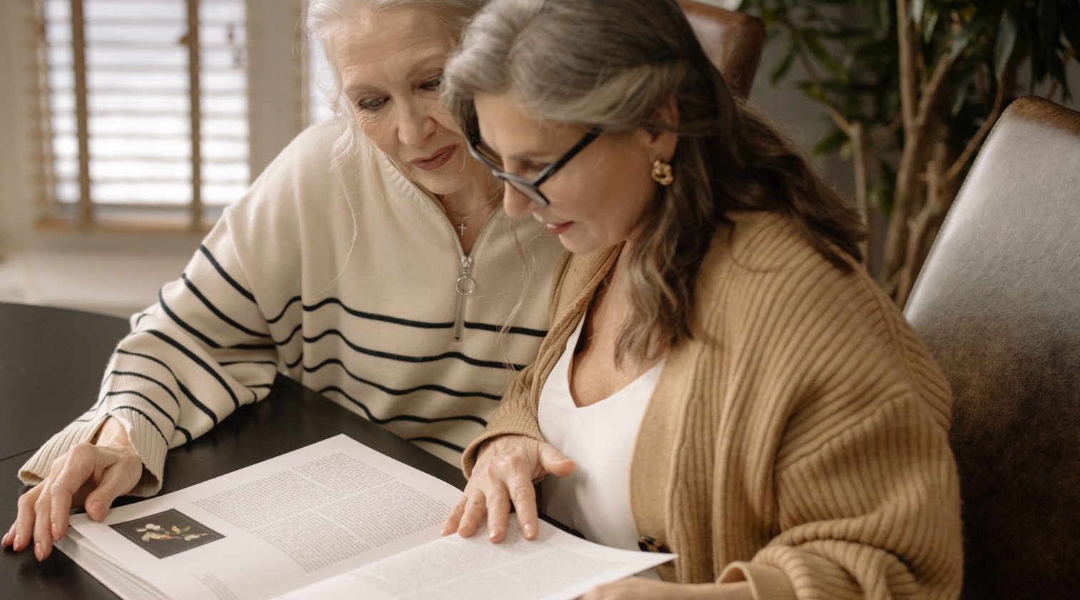 Two women sitting together at a table, looking at an open book